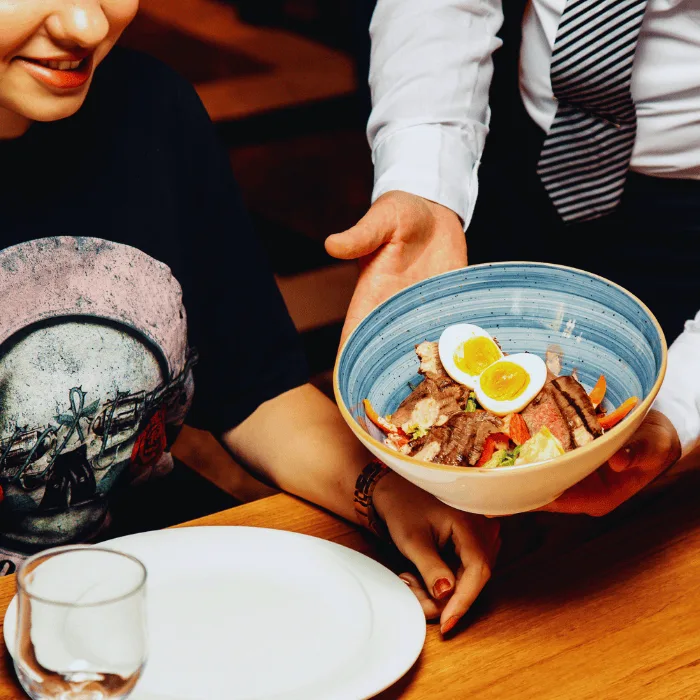 Steak salad with boiled eggs served in a blue ceramic bowl presented at a restaurant setting emphasizing quality and presentation for culinary delights