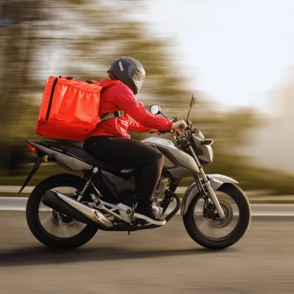 Motorcycle delivery rider in red jacket with large insulated bag riding at high speed on a highway representing fast logistics and delivery services